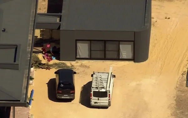 Vue aérienne d'un bâtiment moderne avec des véhicules garés sur un terrain sableux.
