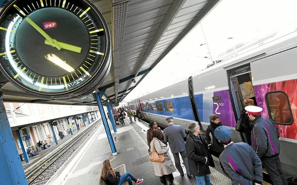 Quai de gare avec une pendule SNCF et des passagers montant dans un train.