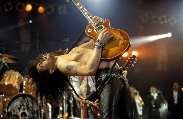 Slash jouant de la guitare électrique torse nu sur scène.