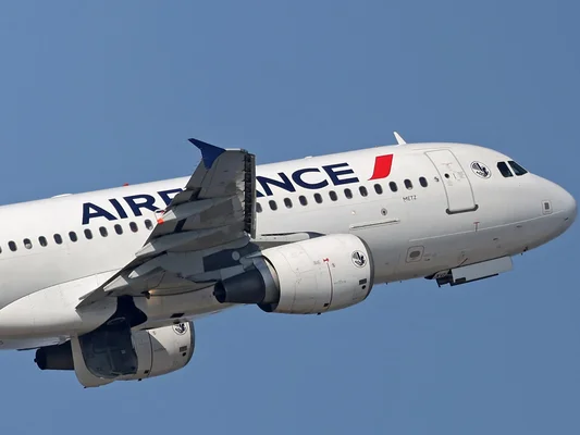 Un avion commercial à l'arrêt sur le tarmac sous un ciel nuageux avec une tour au loin.