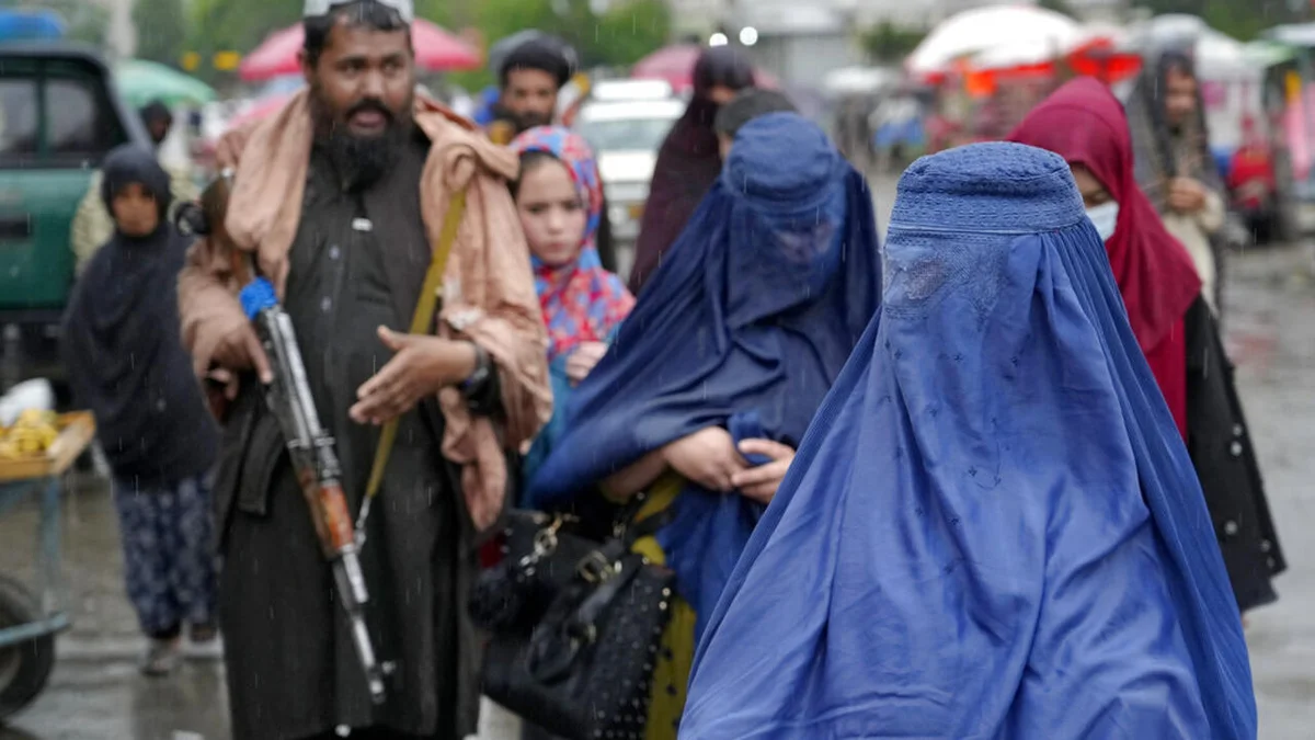 Scène de marché sous la pluie avec deux femmes en burqas bleues et un homme armé à proximité.