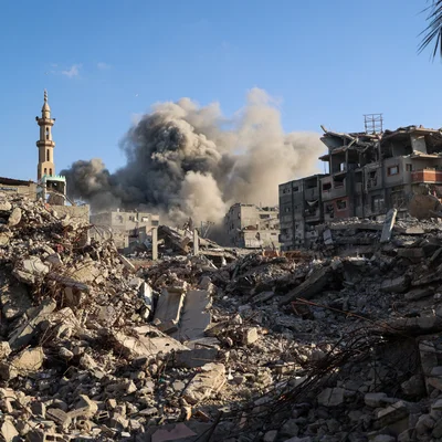Paysage de guerre avec des décombres, des bâtiments en partie détruits et un minaret sous un ciel bleu.
