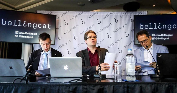Trois enquêteurs lors d'une présentation Bellingcat face au logo de l'organisation.