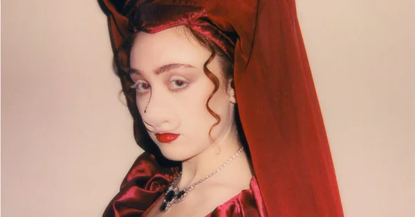 Chappell Roan portant une veste rose et blanche à motifs, posant devant un fond gris.