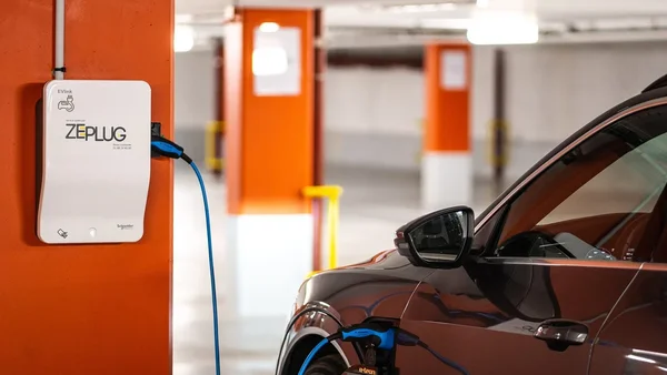 Un véhicule électrique brun relié à une borne ZEPLUG dans un parking intérieur aux piliers orange et blanc.