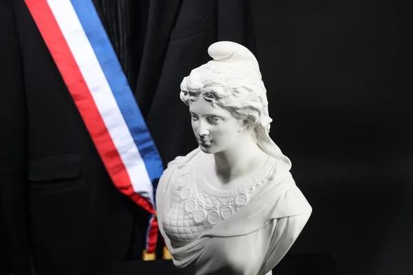 Buste de marbre blanc devant un costume officiel orné de l'écharpe tricolore.