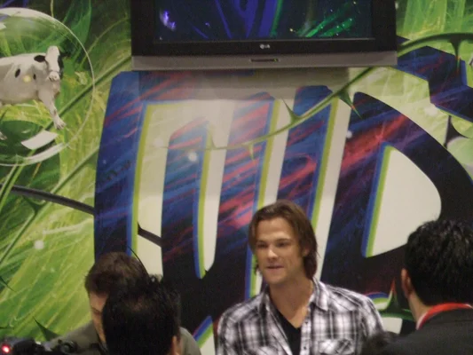 Leighton Meester en robe noire et Jared Padalecki costumé devant un fond événementiel.