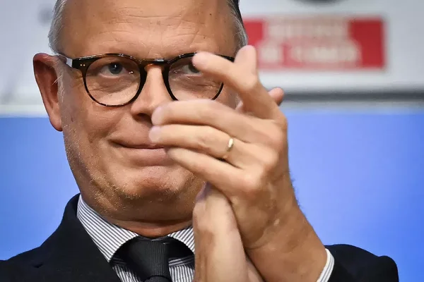 Édouard Philippe en costume et chemise rayée, les mains levées.