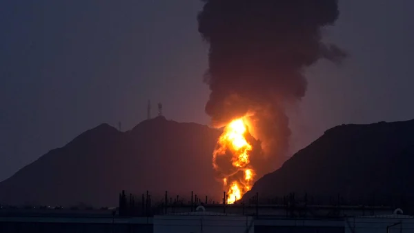 Un camion-citerne détruit et des structures endommagées entourés de fumée noire en Iran.
