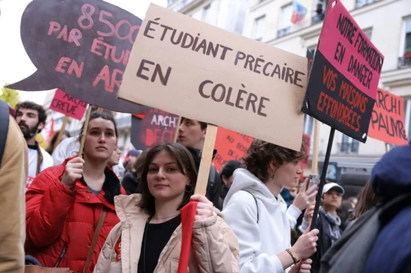 Un jeune homme assis sur des marches en béton, un carnet à la main.