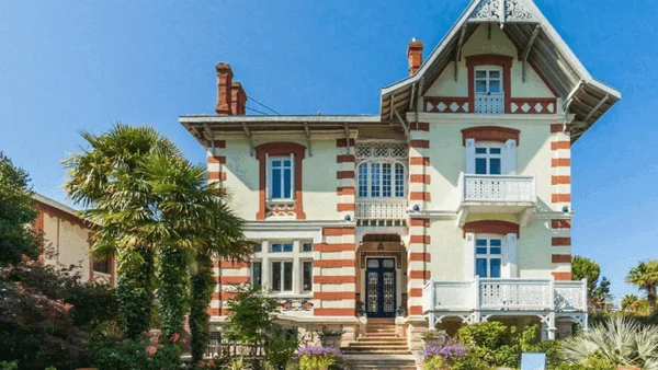 Villa deux étages aux couleurs crème et rouge entourée de palmiers