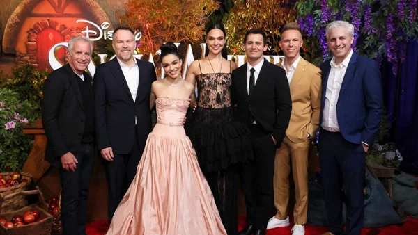 Actrice en costume de scène levant la main dans un décor extérieur aux chaudes lumières bokeh.