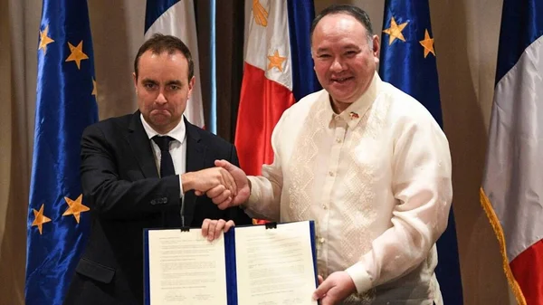 Poignée de main lors de la signature d'un accord entre l'UE et les Philippines, drapeaux en arrière-plan.