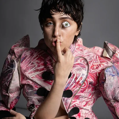 Chappell Roan en corset et gants verts, chantant avec passion le bras tendu devant ses lumières.