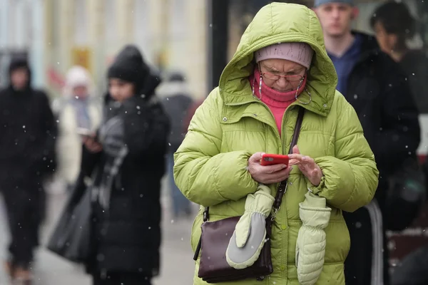 Une personne en doudoune verte regarde un smartphone alors qu'il neige.
