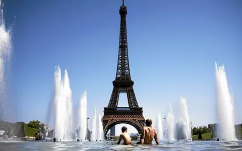 Baigneurs dans une fontaine avec la tour Eiffel en arrière-plan sous un ciel bleu.