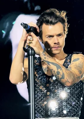 Harry Styles tenant son micro, portant un haut sans manches à motifs circulaires.