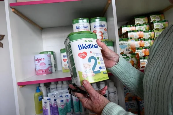 Une personne tenant une boîte de lait infantile Bledilait devant des rayons de produits pour bébé.