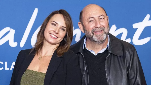 Julia Vignali et Kad Merad posent ensemble devant un fond bleu.