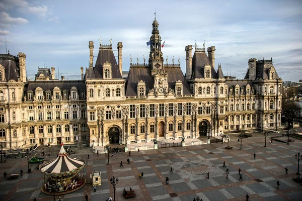 L'Hôtel de Ville et sa place animée, avec un manège installé devant la façade officielle.