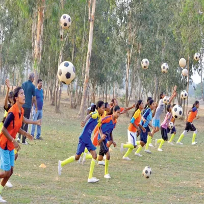 Des jeunes filles en uniforme sportif jouent au football sous le regard d'adultes.