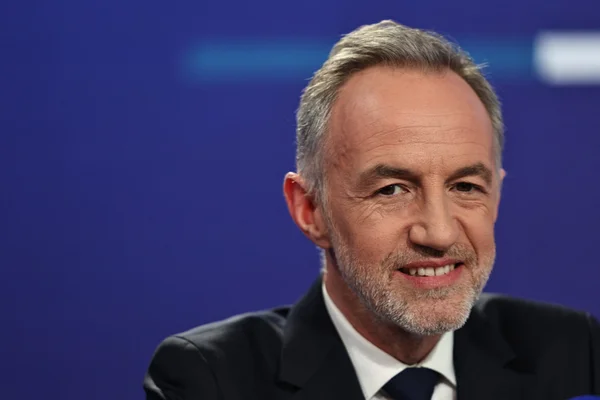 Portrait d'Emmanuel Grégoire souriant en costume sur fond bleu, en tête des sondages à Paris.