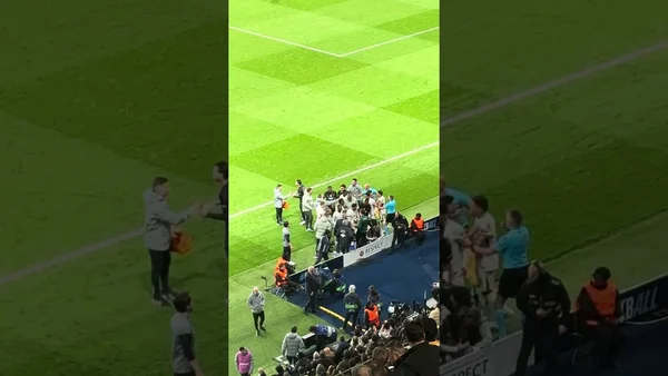 Regroupement de joueurs et staff sur la touche du terrain durant une rencontre, avec des spectateurs en arrière-plan.