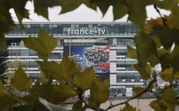 Le siège de France.tv affichant le logo sur sa façade vitrée, entouré de végétation.