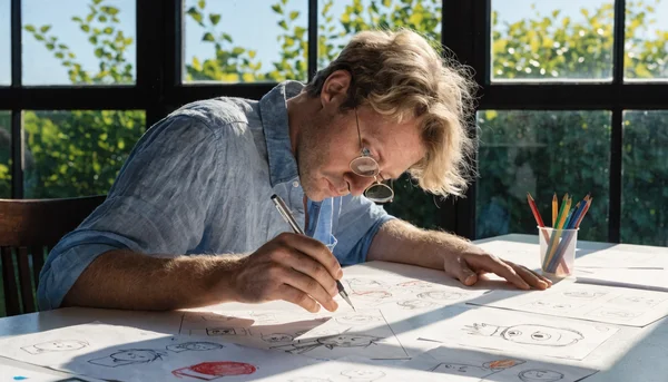 Un homme au visage rond avec de petites lunettes travaillant à un bureau lumineux, une mine de crayon à la main, concentré sur des planches de dessin d'animation éparpillées