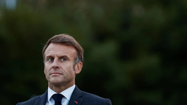 Le président Emmanuel Macron en costume, au regard sérieux, posant devant un fond vert.