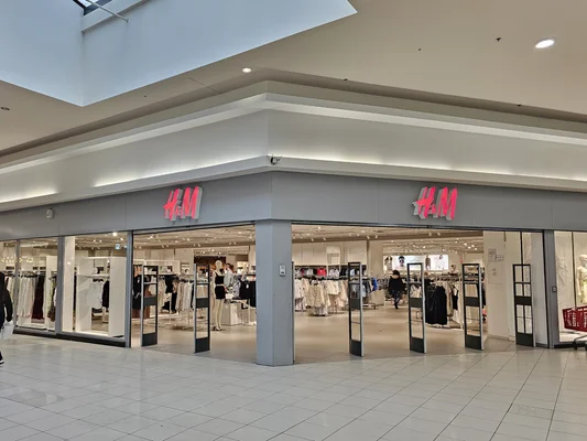L'entrée du magasin H&M au Shopping Cora de La Louvière en Belgique, identifiable par son enseigne rose caractéristique.