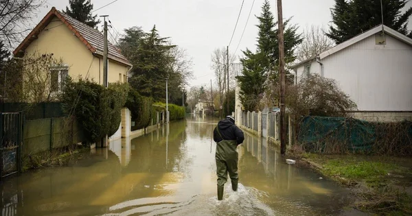 Un résident équipé de waders s'avance dans l'eau d'une rue inondée.