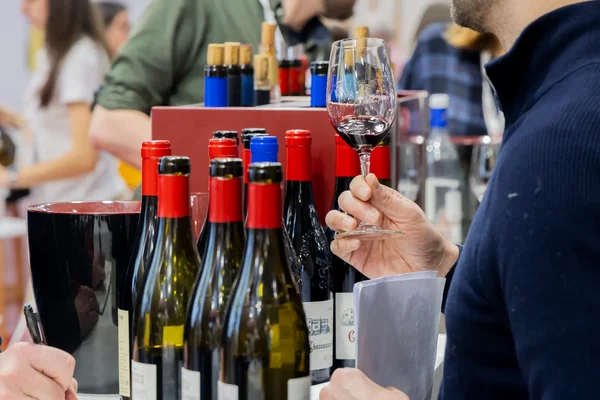 Une personne tenant un verre de vin rouge, entourée de bouteilles lors d'une dégustation.