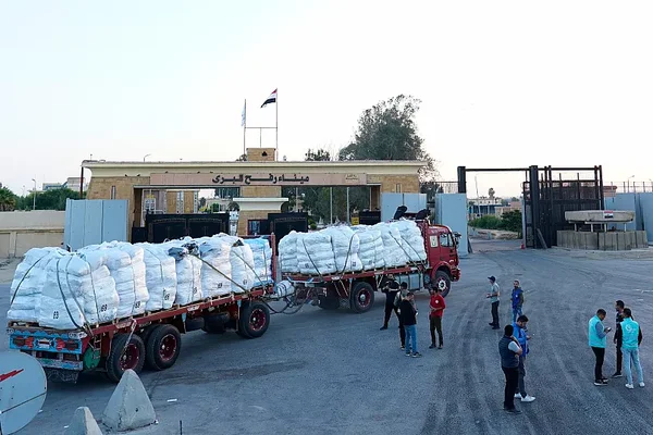 Camions à un poste-frontière entre Gaza et l'Égypte, avec des drapeaux et des panneaux.