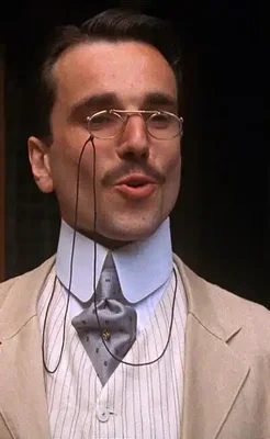 Daniel Day-Lewis en veston beige et lunettes rondes, portrait sur fond sombre.