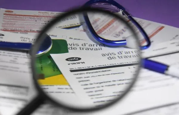 Un formulaire d'arrêt de travail examiné à la loupe, stylo et lunettes à côté.