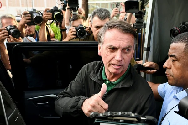 Jair Bolsonaro saluant la presse d'un pouce en l'air au milieu des photographes.