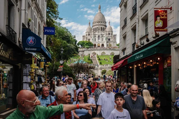 Vue à travers l'arche de la Tour Eiffel montrant un parc fréquenté par des touristes avec des bâtiments historiques en arrière-plan.