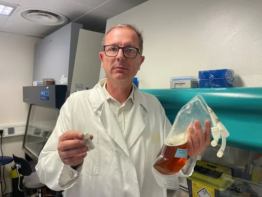 Un scientifique tenant des solutions en laboratoire devant du matériel technique.