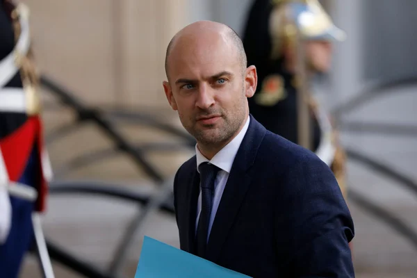 Jean-Noël Barrot tenant un dossier bleu, accompagné de gardes.