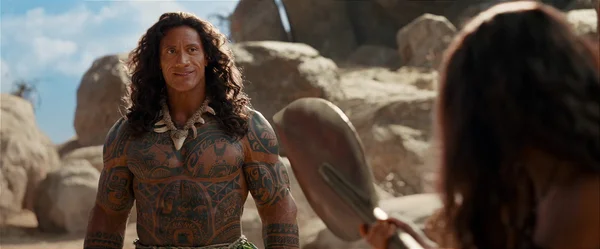 Dwayne Johnson en Maui avec son collier d'os, dans un décor rocheux, avec un personnage tenant une rame à l'avant-plan.