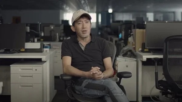 Shinji Mikami assis dans un environnement de bureau avec des équipements informatiques.