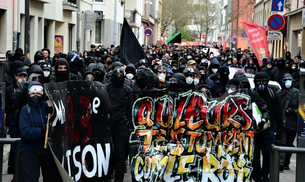 Manifestants masqués en tenue noire marchant dans les rues de Strasbourg avec des boucliers et une bannière.