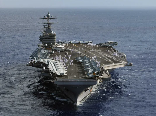 Le porte-avions USS Abraham Lincoln avec des avions de chasse alignés sur le pont d'envol et du personnel en uniforme naviguant en haute mer.