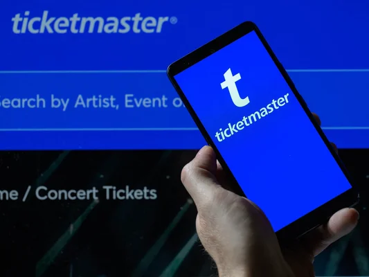 Une main tenant un téléphone montrant l'application et le logo de Ticketmaster.