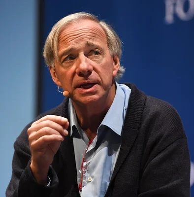 Ray Dalio lors d'une intervention publique, portant une chemise bleue claire et des lunettes posées sur son shirt.