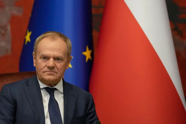 Donald Tusk assis devant le drapeau de l'Union européenne et le drapeau polonais.