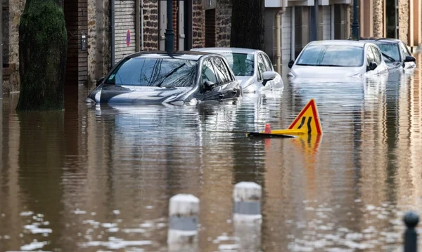 Une rue urbaine sous les eaux avec un panneau de signalisation flottant et des véhicules.