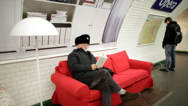 Un lecteur concentré sur un canapé rouge installé dans la station de métro Opéra à Paris.