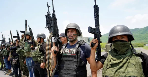 Membres armés d'un cartel en tenue tactique, avec un homme portant un gilet 'DELTA'.